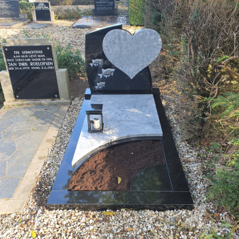 Grafmonument met een wit hart en vissen op de steen. Deze grafsteen is van zwart en wit graniet en heeft een tuin